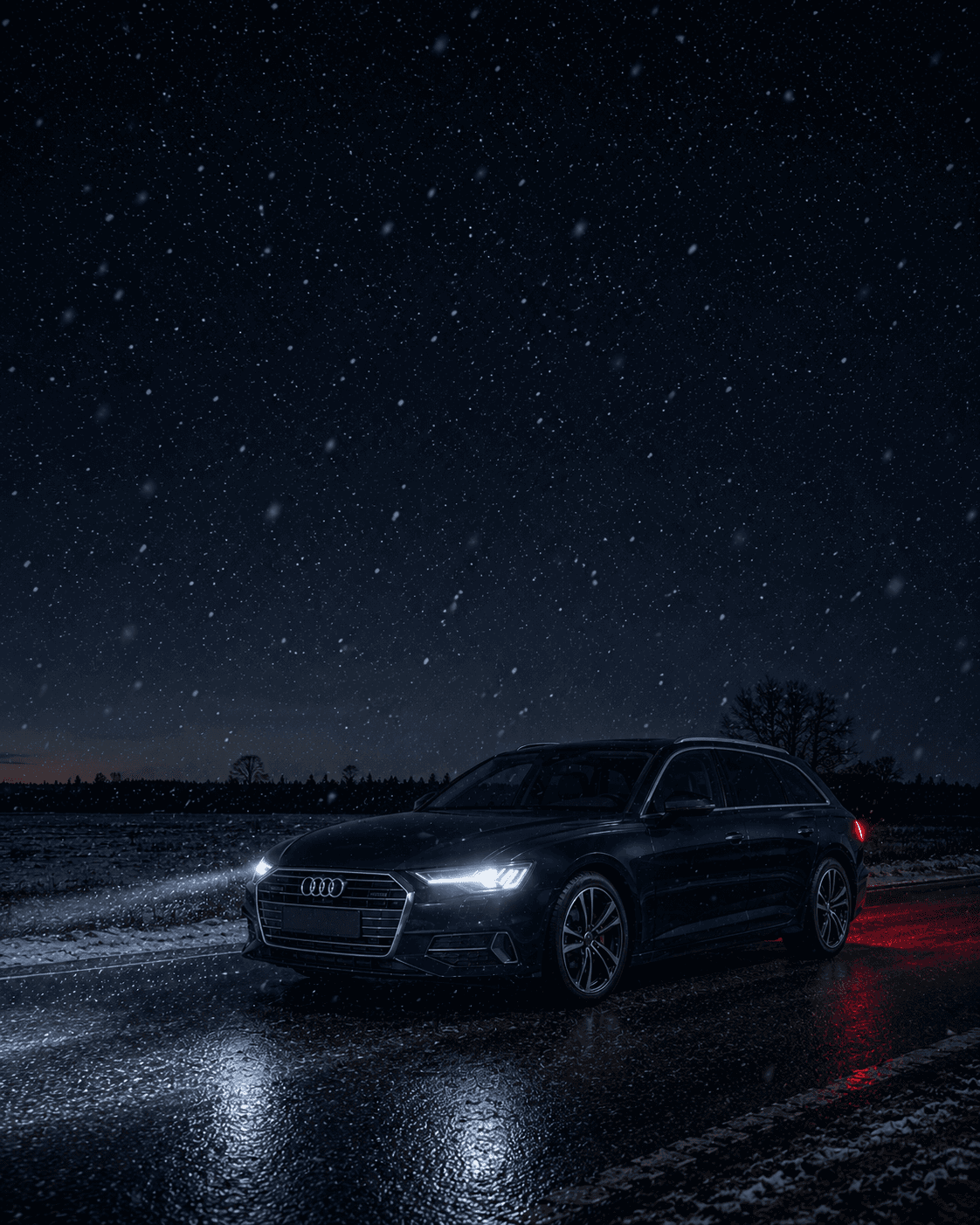 Mörkblå Audi A6 Avant med tända strålkastare på en mörk vinterväg tidig morgon